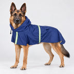 A German Shepherd wearing a navy blue dog raincoat with bright green reflective trim, standing against a seamless white studio background.