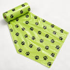 A roll of bright lime green plastic bags printed with a repeating black paw print pattern, shown partially unrolled on a plain white background.